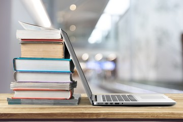 A stack of books beside a laptop on a wooden desk